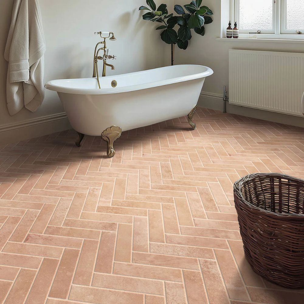 A bathroom floor featuring slim terracotta-toned tiles laid in a herringbone pattern. The tiles have a soft, matt finish that complements the clawfoot bath and neutral wall colour.