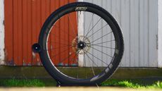 Zipp 303 Firecrest wheel in a wheel stand pictured against a red and grey wooden door