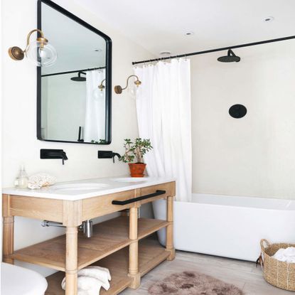 double hand basin in a wooden vanity unit with a black rimmed mirror above and a bath and white shower curtain