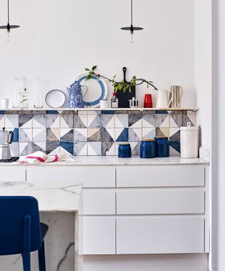White kitchen with colorful blue and white backsplash tiles, sleek cabinetry and open shelving.