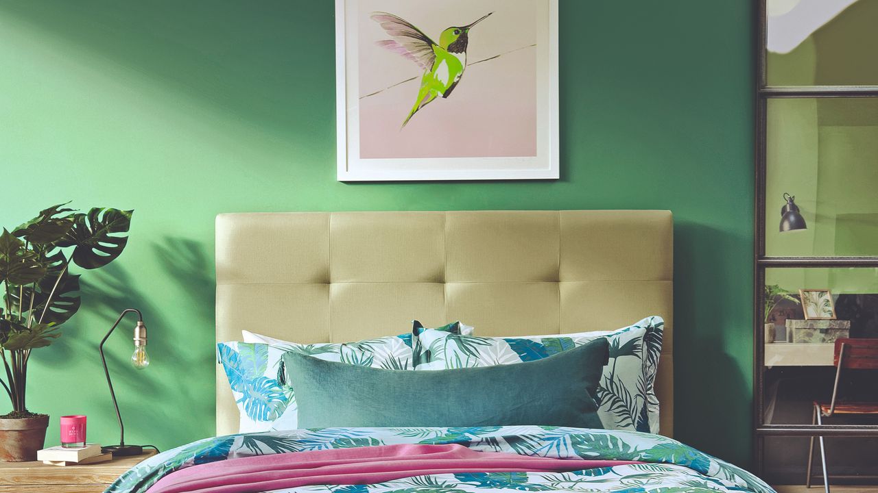 A green-painted bedroom with tropical bed linen on the bed