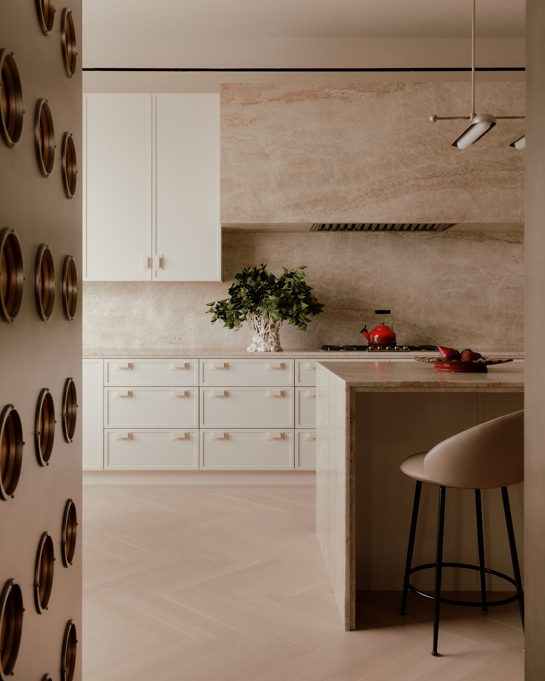 modern neutral kitchen with white cabinets, marble walls, parquetry floors, a kitchen island and brown bar stool