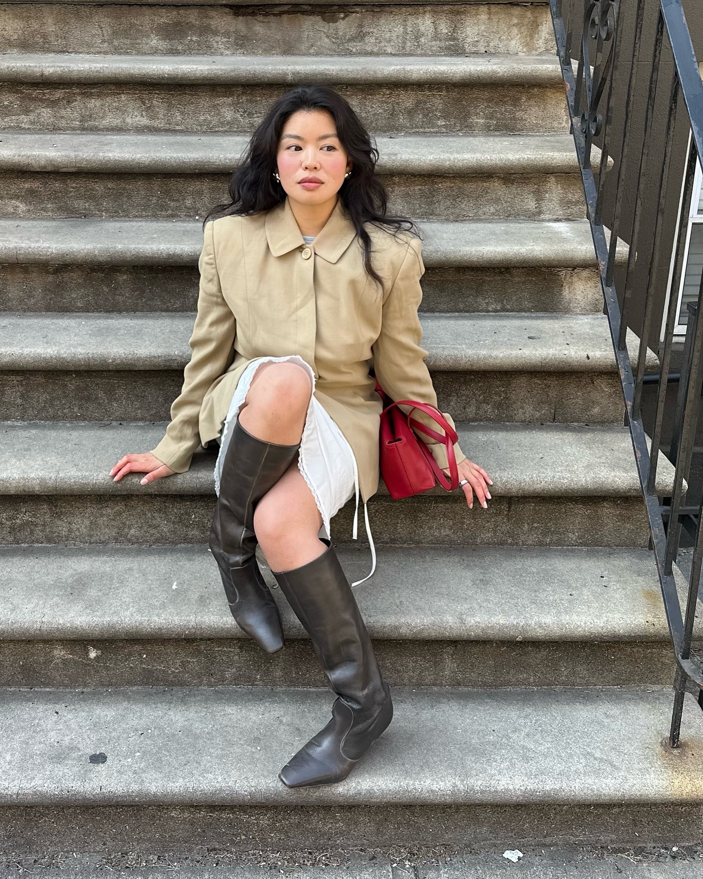 A woman sitting on the steps leading up to an apartment in a stylish outfit with a bouncy hairstyle