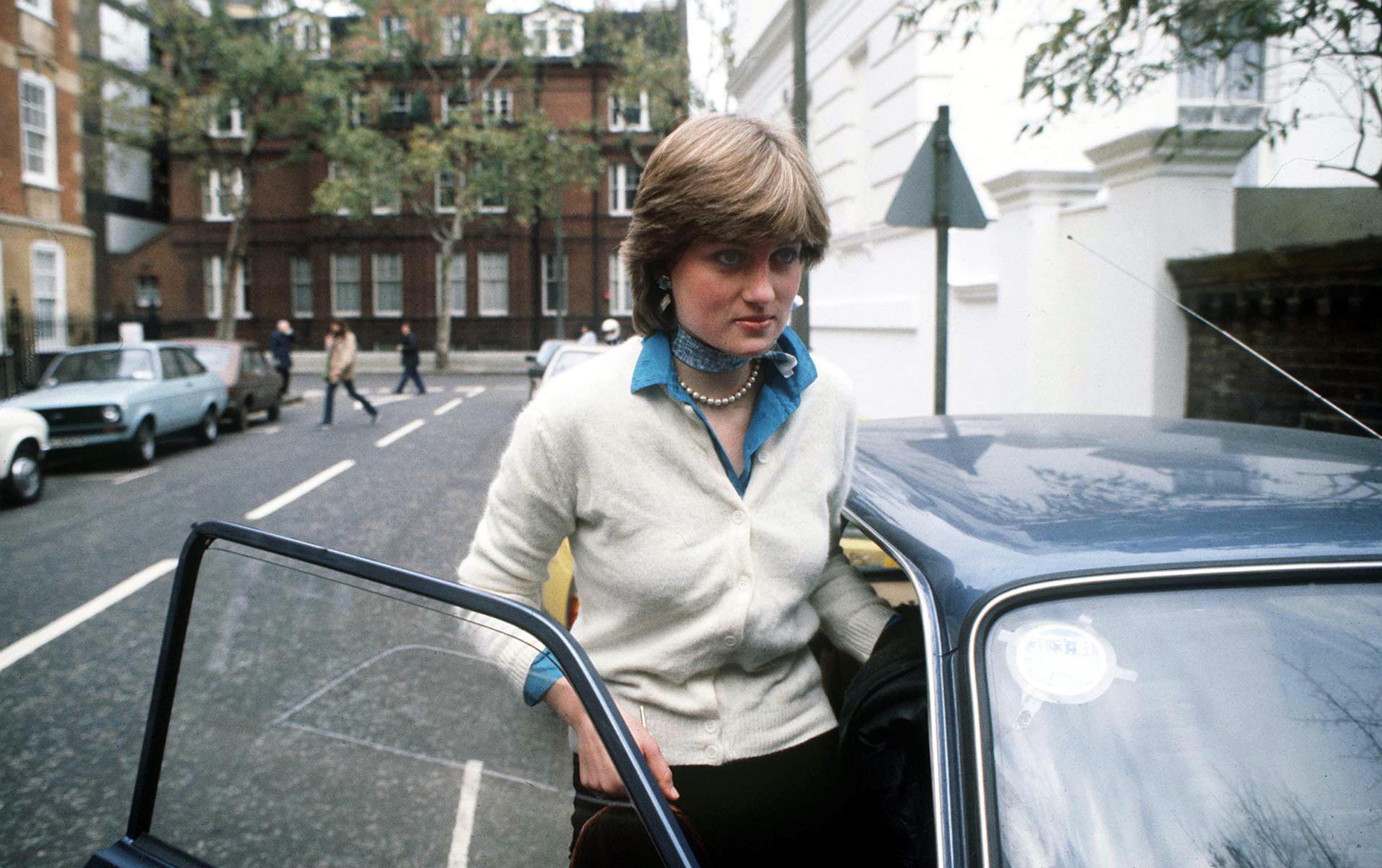 Princess Diana wearing a white cardigan getting into a car