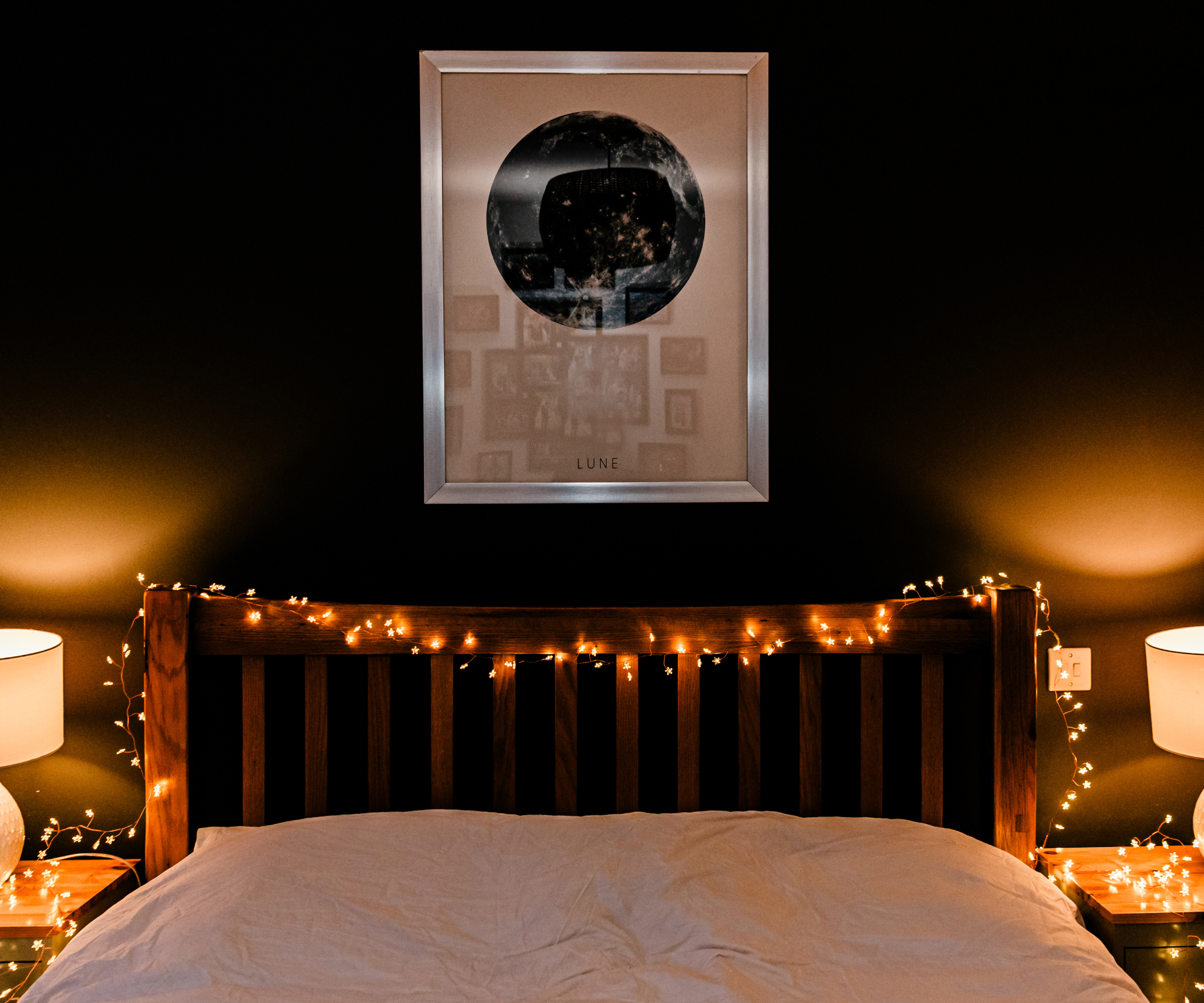bed with fairy lights draped across frame, two small bedside lights either side of bed
