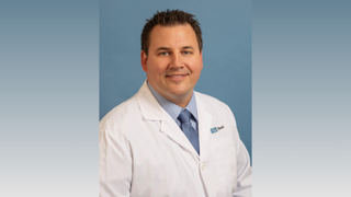 Picture of Dr. Thomas Kremen against a gradient blue and white background. He is wearing a blue shirt, blue tie and white physician coat and smiling at the camera.