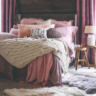 A bedroom with cosy, textured bedding layered on top of the bed and rugs layered on the floor