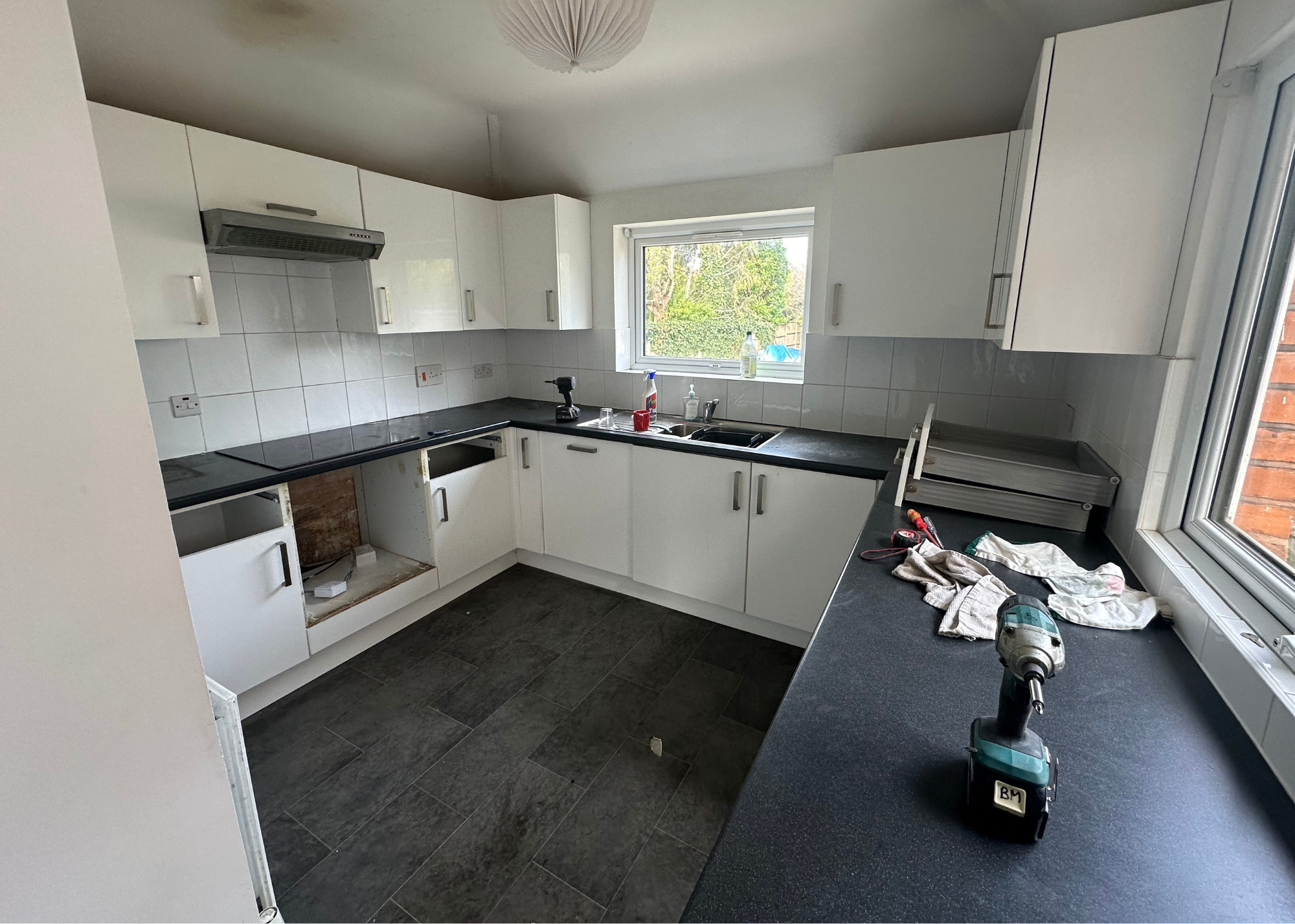 a before shot of a rundown, old fashioned kitchen with white cabinets, dark counters and white tiles