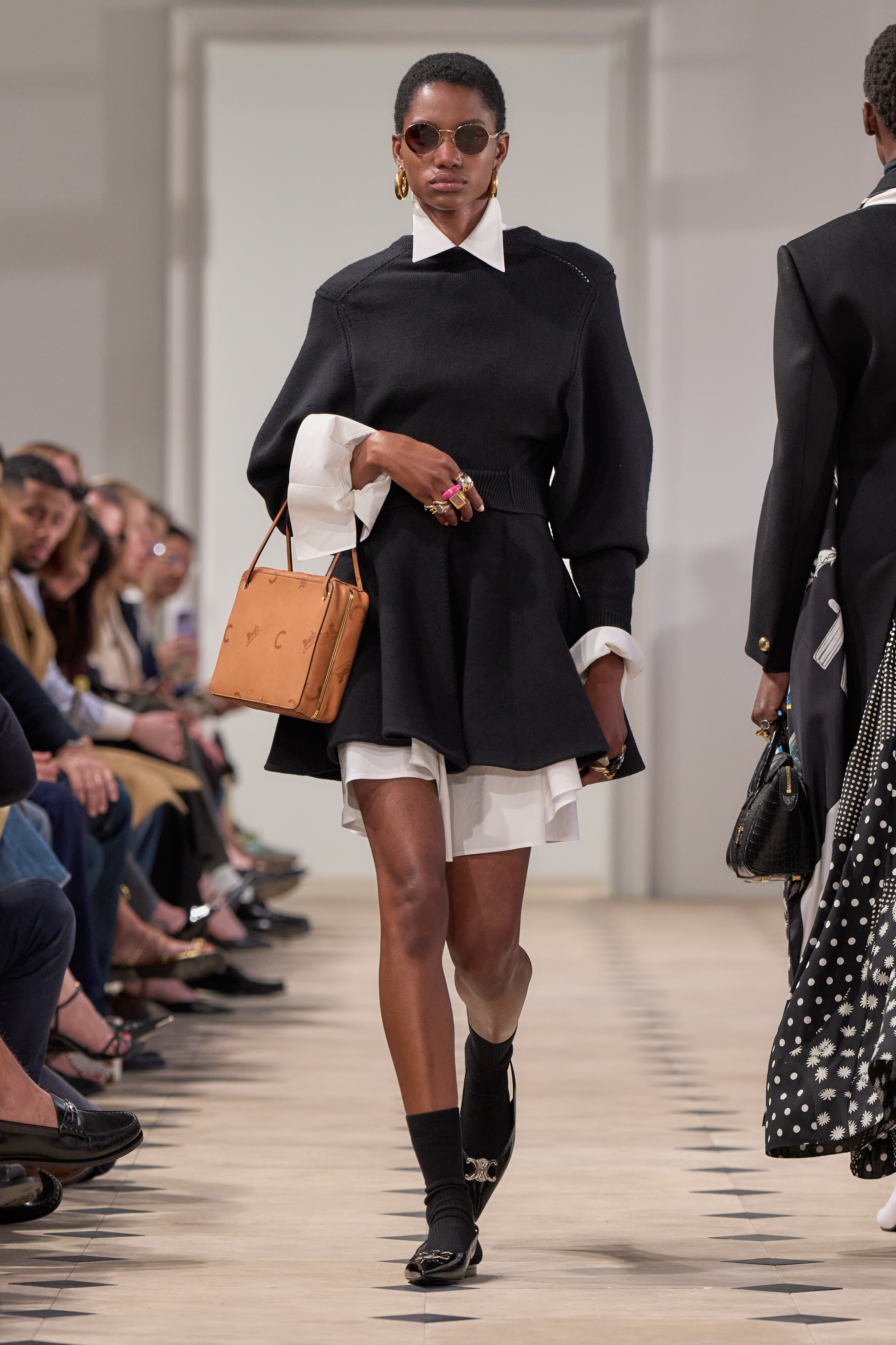 a model walks the runway at Celine wearing a black layered dress and a celine logo bag