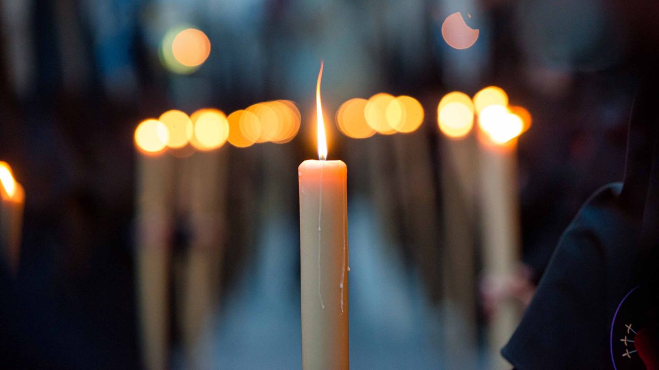 one candle lit in focus with several candles lit that are blurred