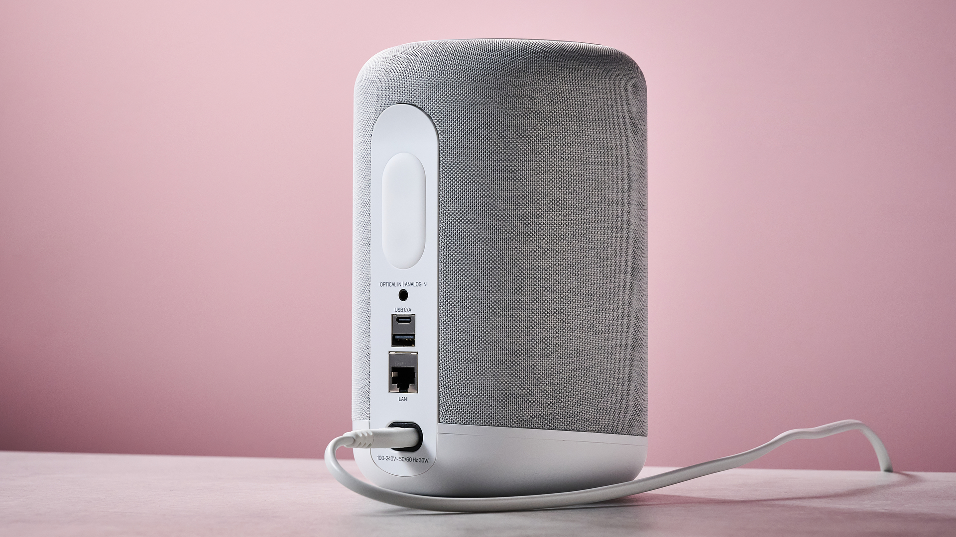 The Bluesound Pulse Flex from behind on a stone effect counter in front of a pink background.