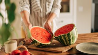 Woman with full size watermelon sitting on chopping board, about to cut the fruit with a knife