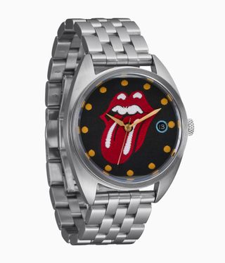 A silver watch with a tongue sticking out of red lips on a black face with yellow hands.