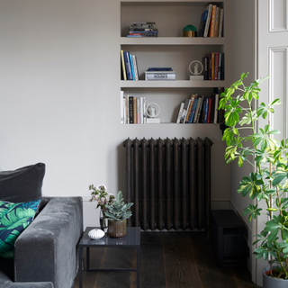 helving built into a corner alcove below elaborate coving with a dark metal radiator and dark wooden flooring.