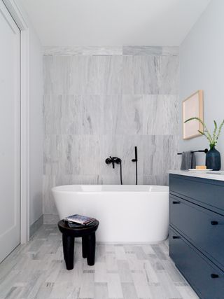 grey tiled bathroom with white tub, hand shower, navy vanity
