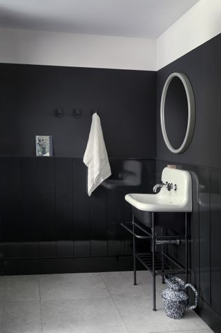 An example of dark bathroom ideas showing a black bathroom with a white ceiling and black painted panelling with a gray tiled floor