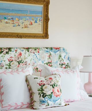 bedroom with white walls and chintz headboard and pretty pink edged cushions and coastal picture above bed