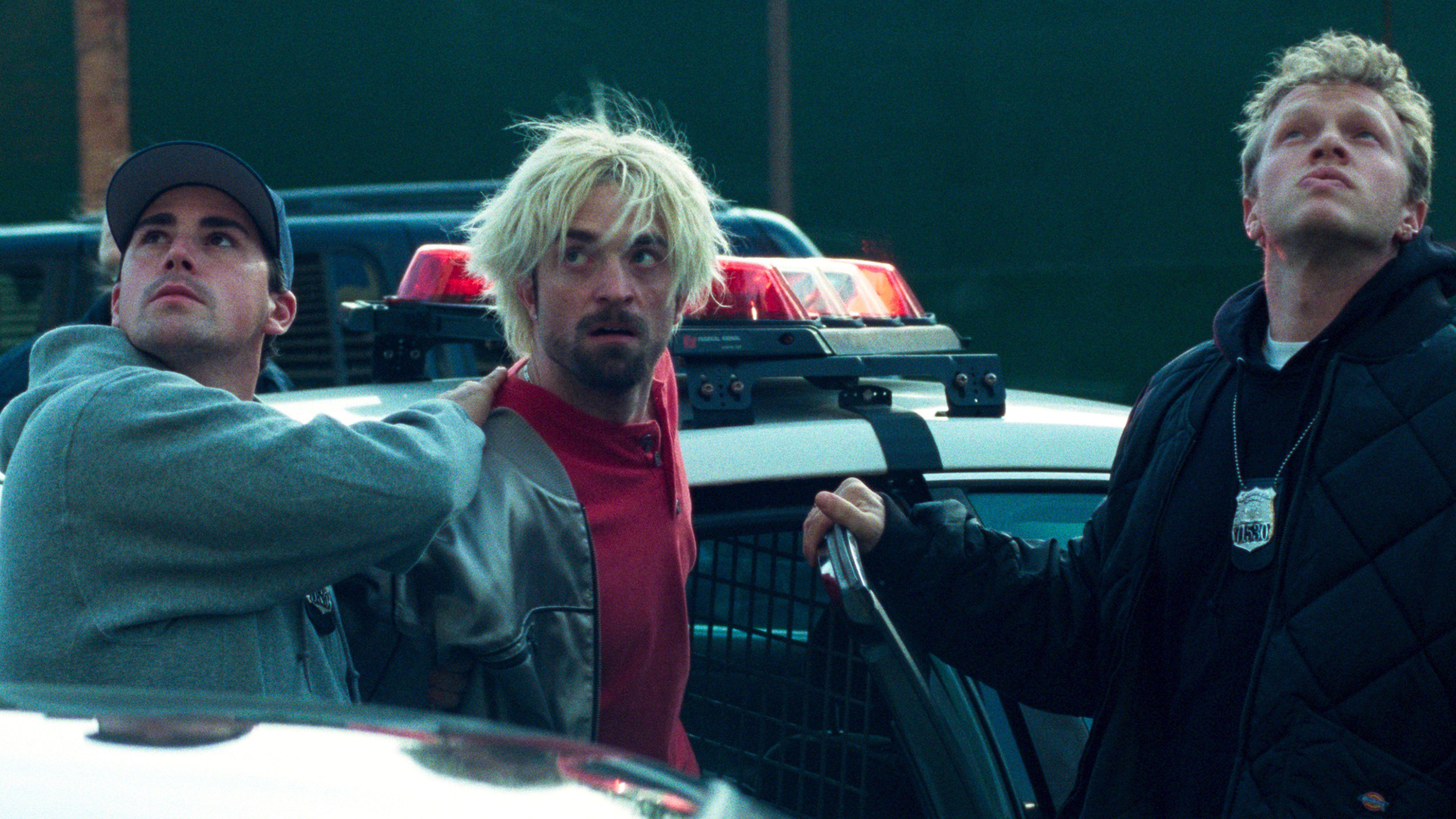 Connie (Robert Pattinson, center) being held by police officers in a scene from "Good Time"