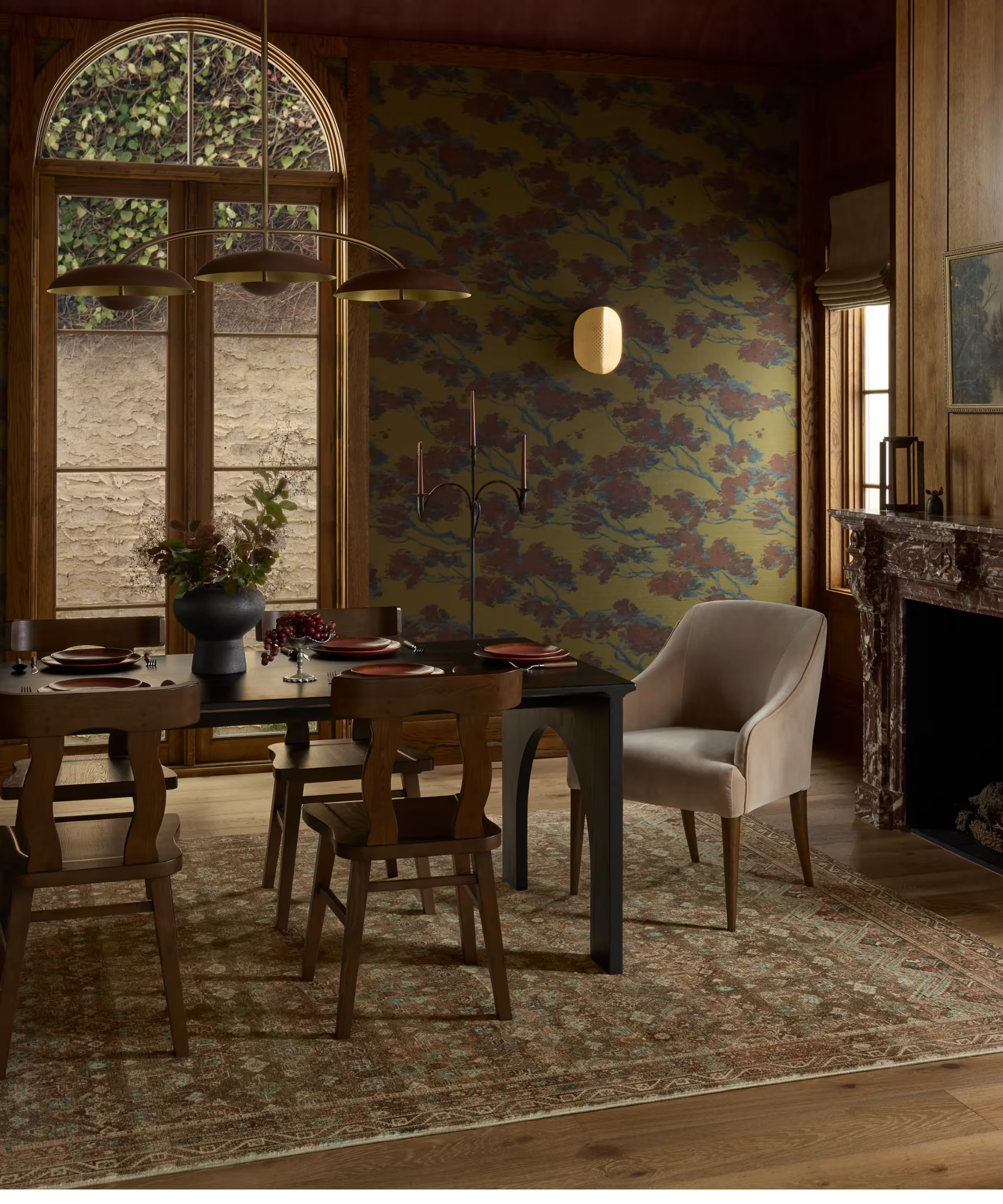 a dining room with a large vintage-inspired area rug, a wood dining table with dining chairs surrounding it, and floral wallpaper on the walls
