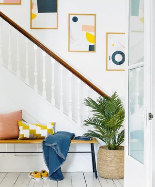 white hallway with wooden topped bannisters and colourful cushions on bench next to potted plant