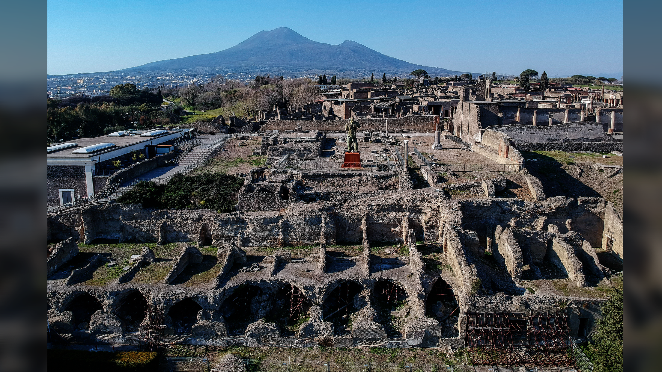 a drone shot of the ruins of Pompeii with Vesuvius rising up in the background against a clear blue sky