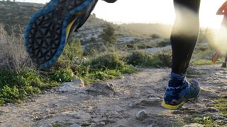 Close-up of person's shoes running on rocky trail