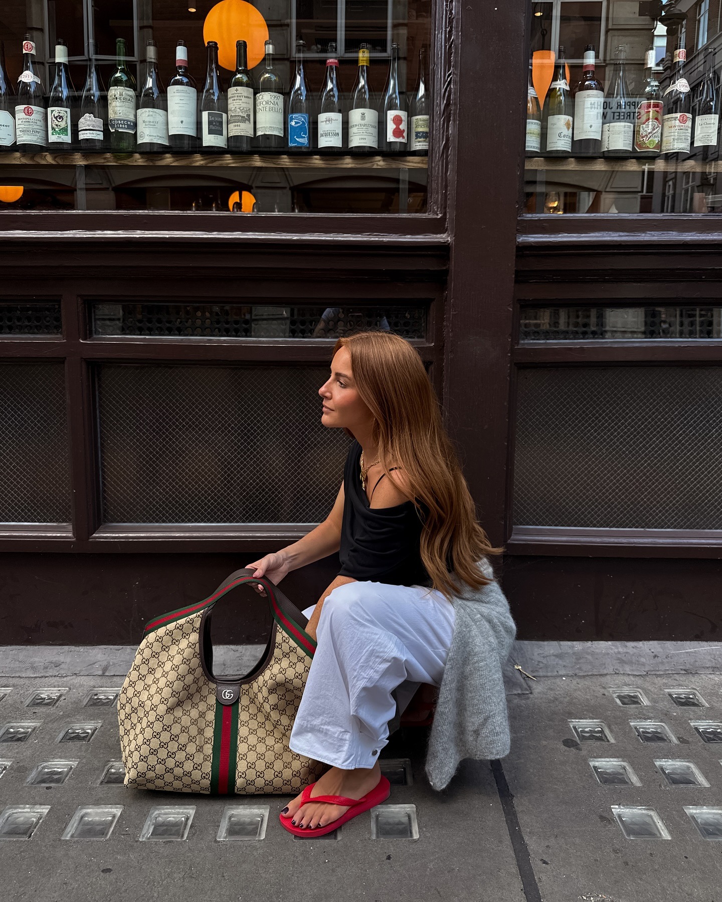 Woman wears black top, white trousers, flip flops and gucci bag