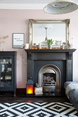 A pink living room with black fireplace and bold monochrome rug, a large mirror over the fireplace and a dark black cabinet