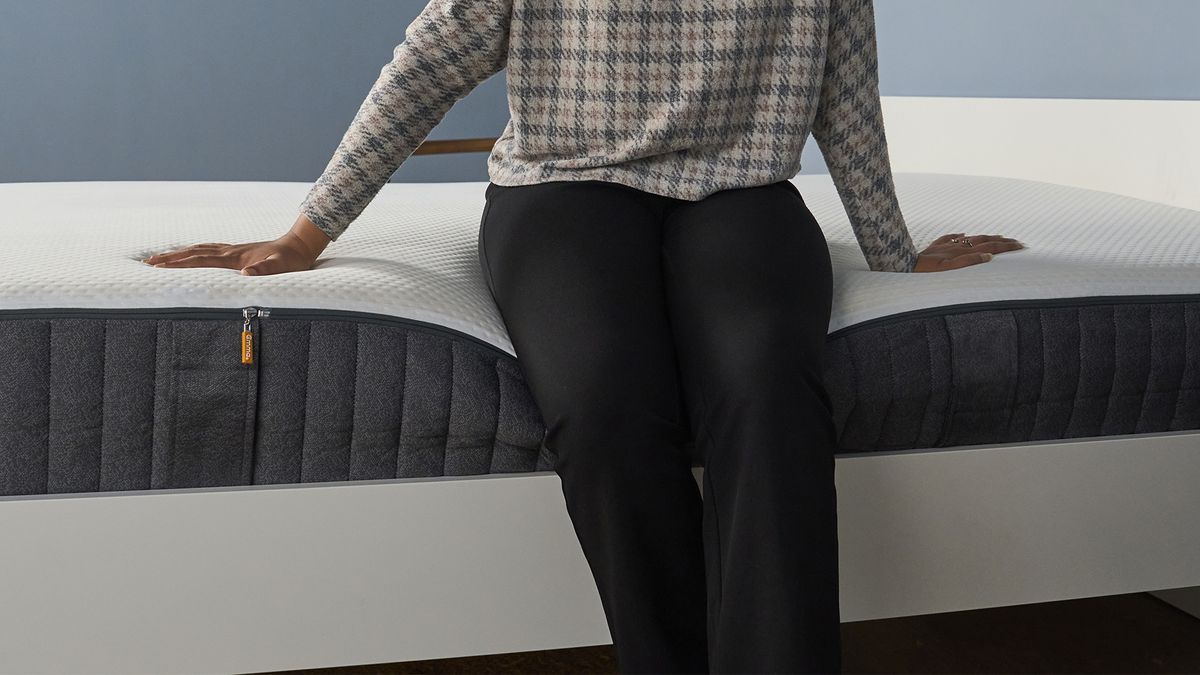 A person sits on the edge of the Emma Hybrid Airgrid Mattress to test the support and comfort