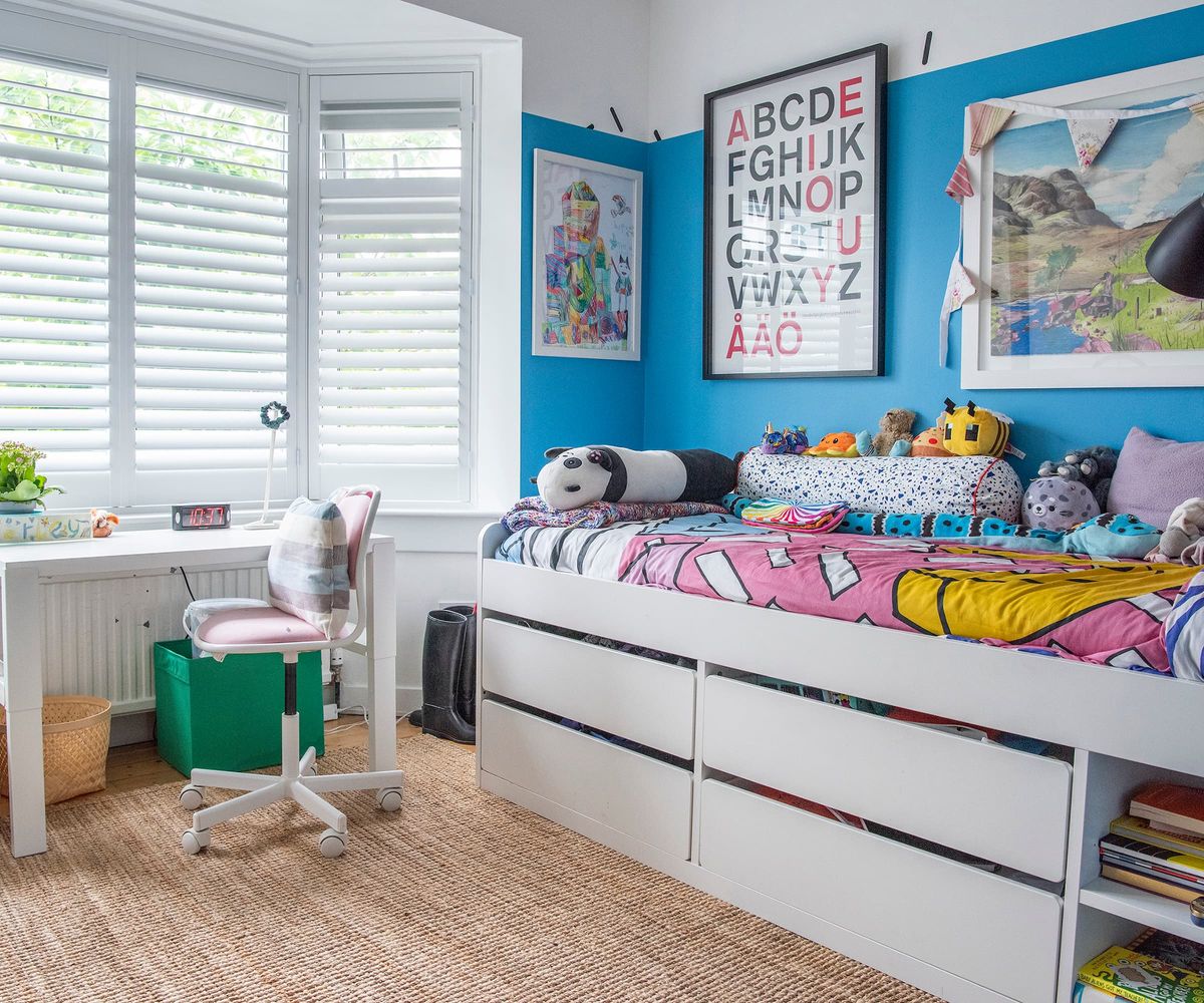 A child's bedroom with under bed storage spaces a desk and art filled walls