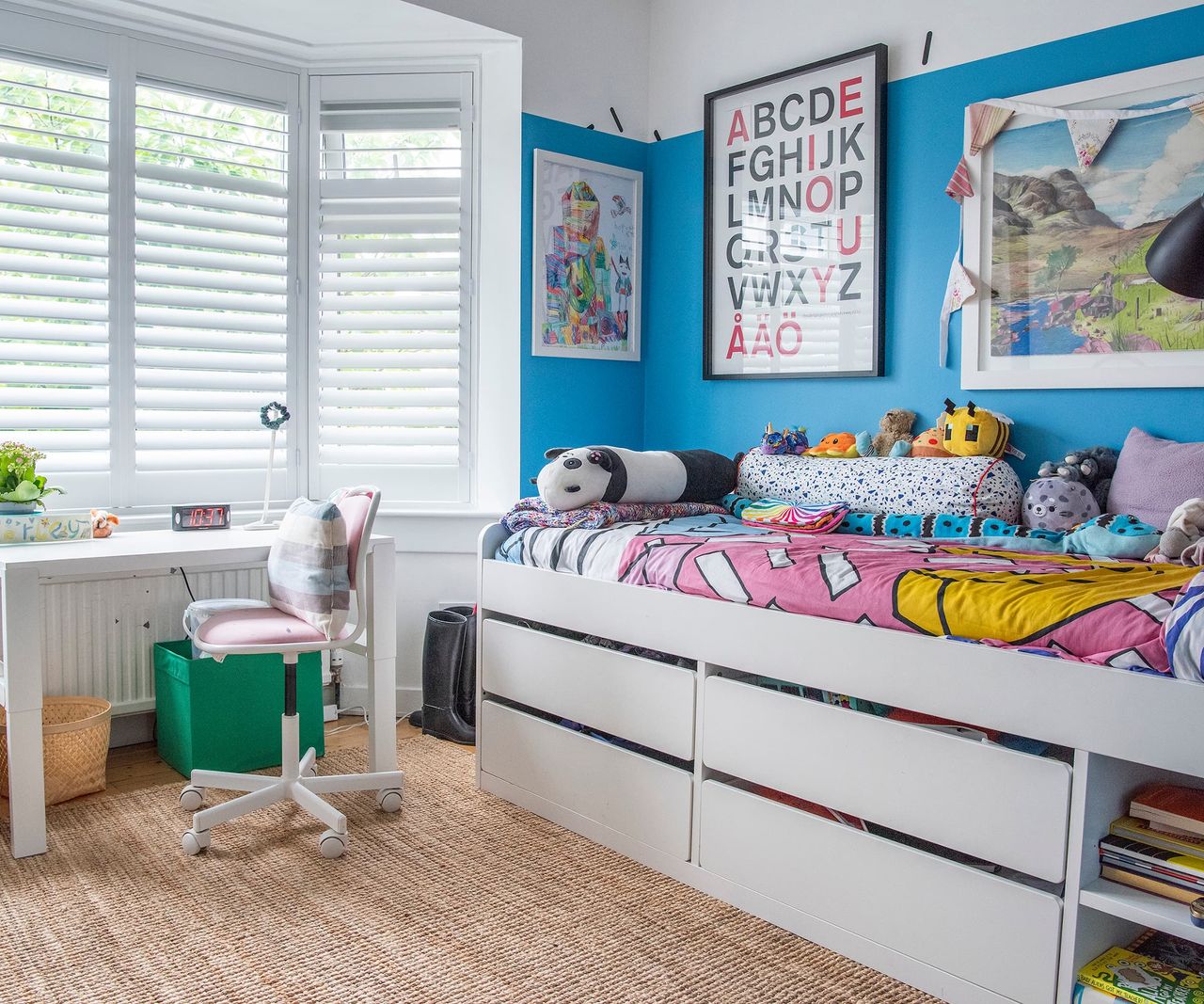 A child's bedroom with under bed storage spaces a desk and art filled walls