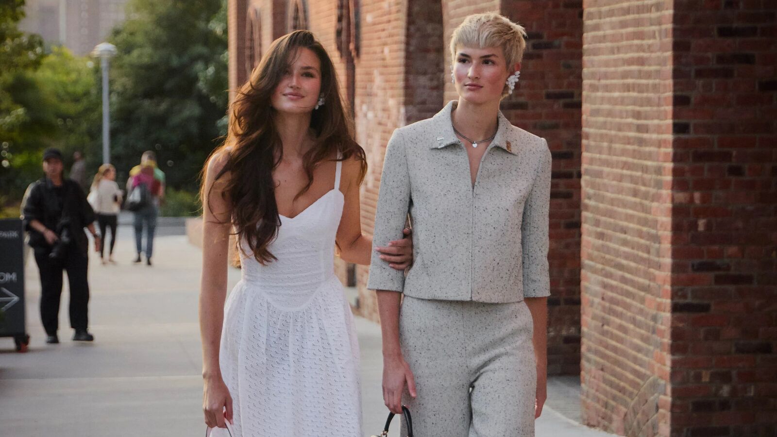 Two people are walking and posing together. One is wearing a white dress and another is wearing a capri matching suit set. 