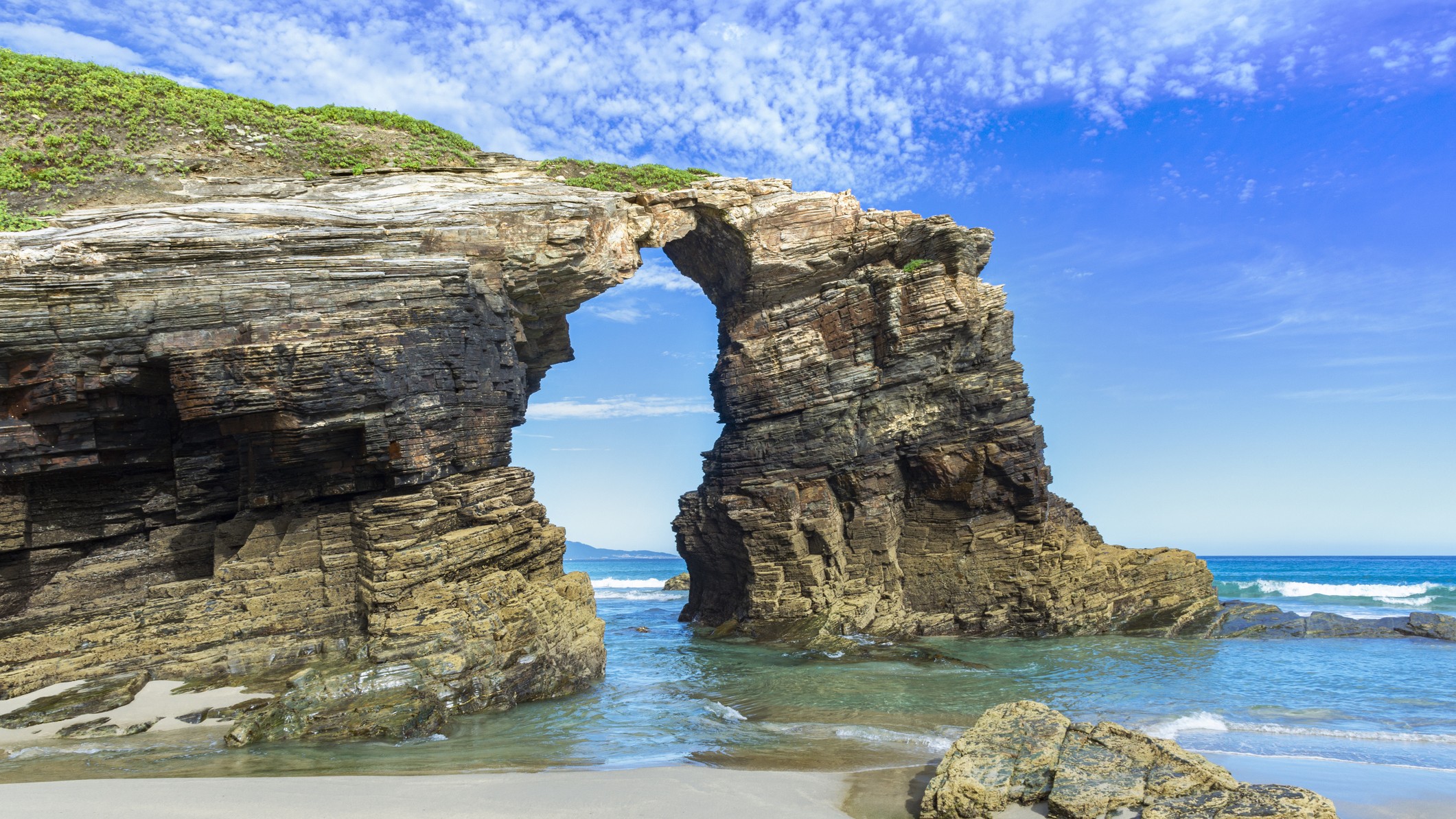 impressive looking rock structure in the shape of an arch. deep blue sky above and light blue waters below.