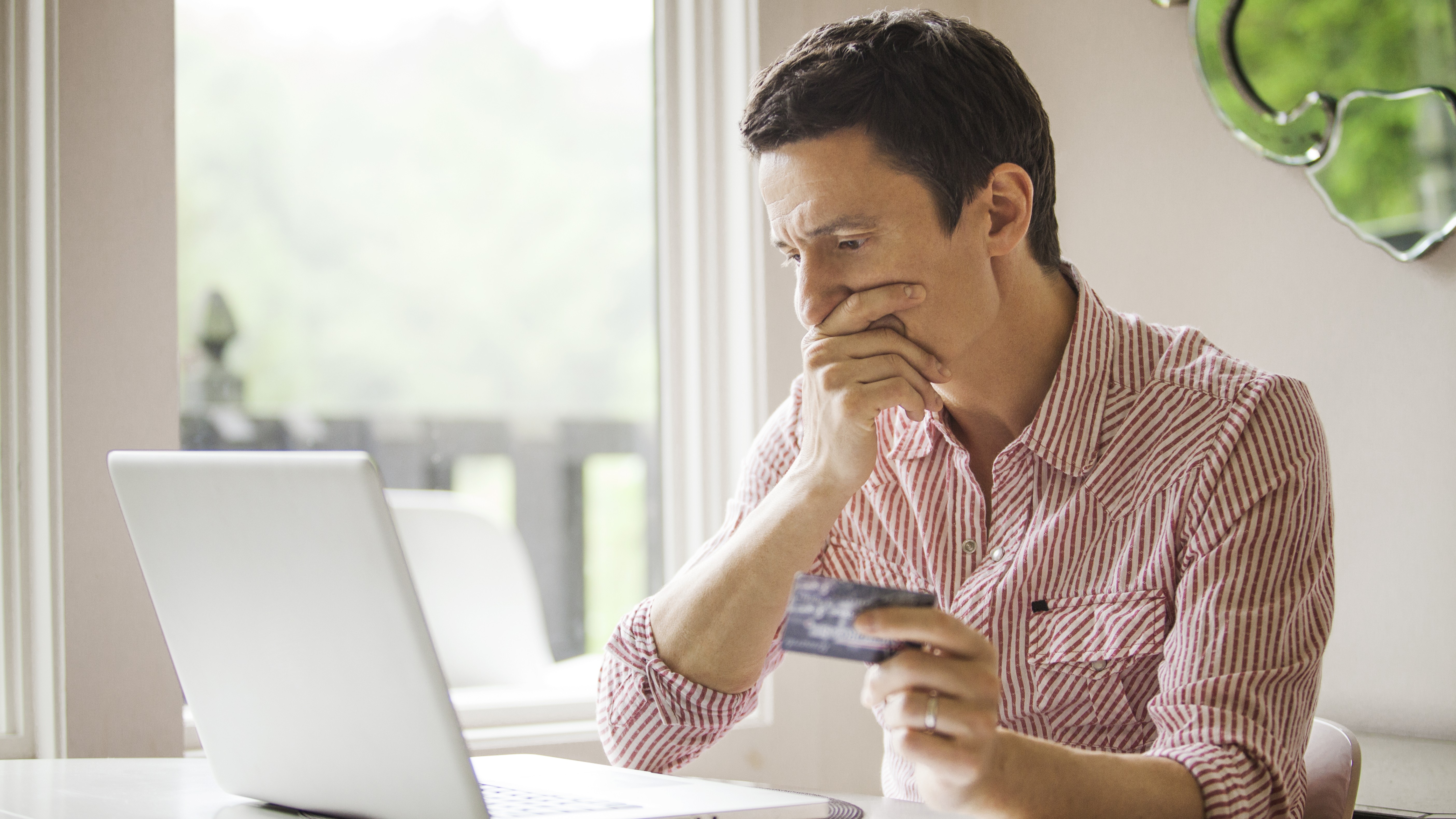 Man holding credit card, looking thoughtfully at laptop screen