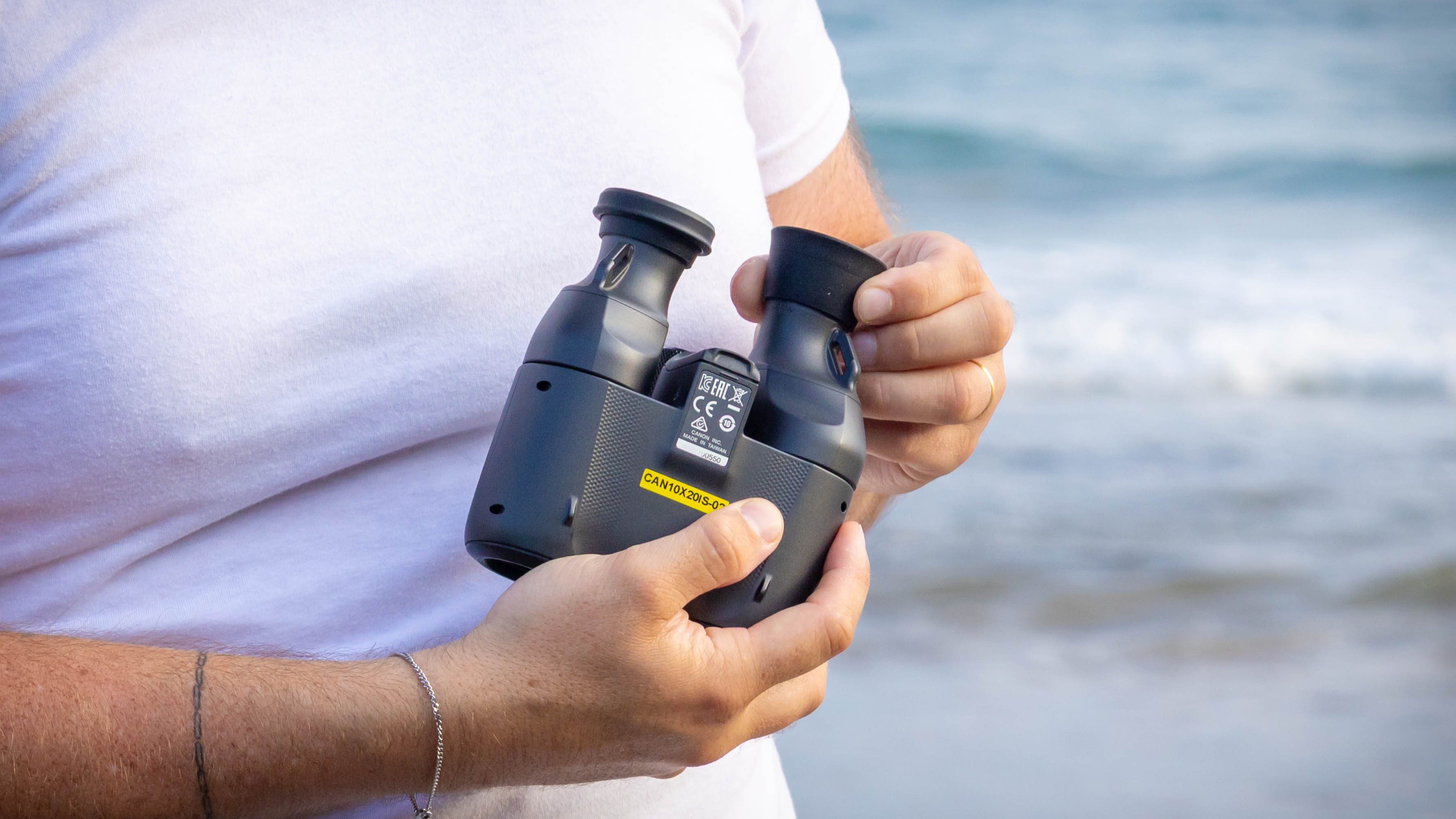 The underside of the Canon 10x20 IS binoculars, being shown by a person.