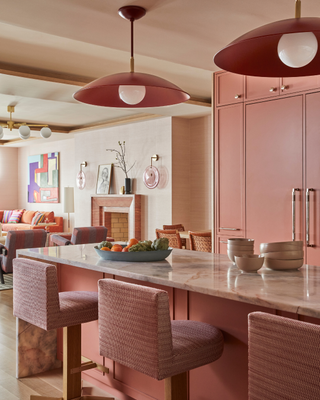 pink kitchen with pink cupboards, pink bar stools, marble counter, gallery wall in background