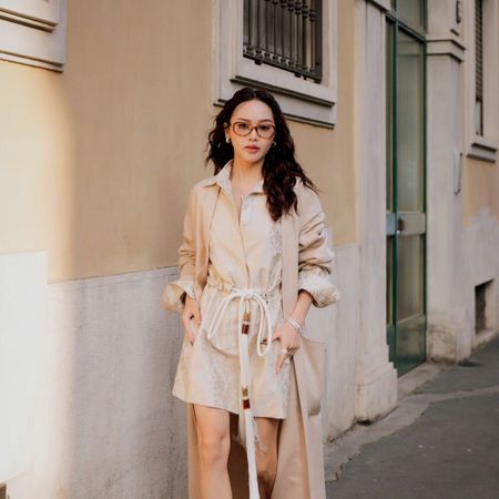Woman wears trench coat with shirt dress in Milan. 