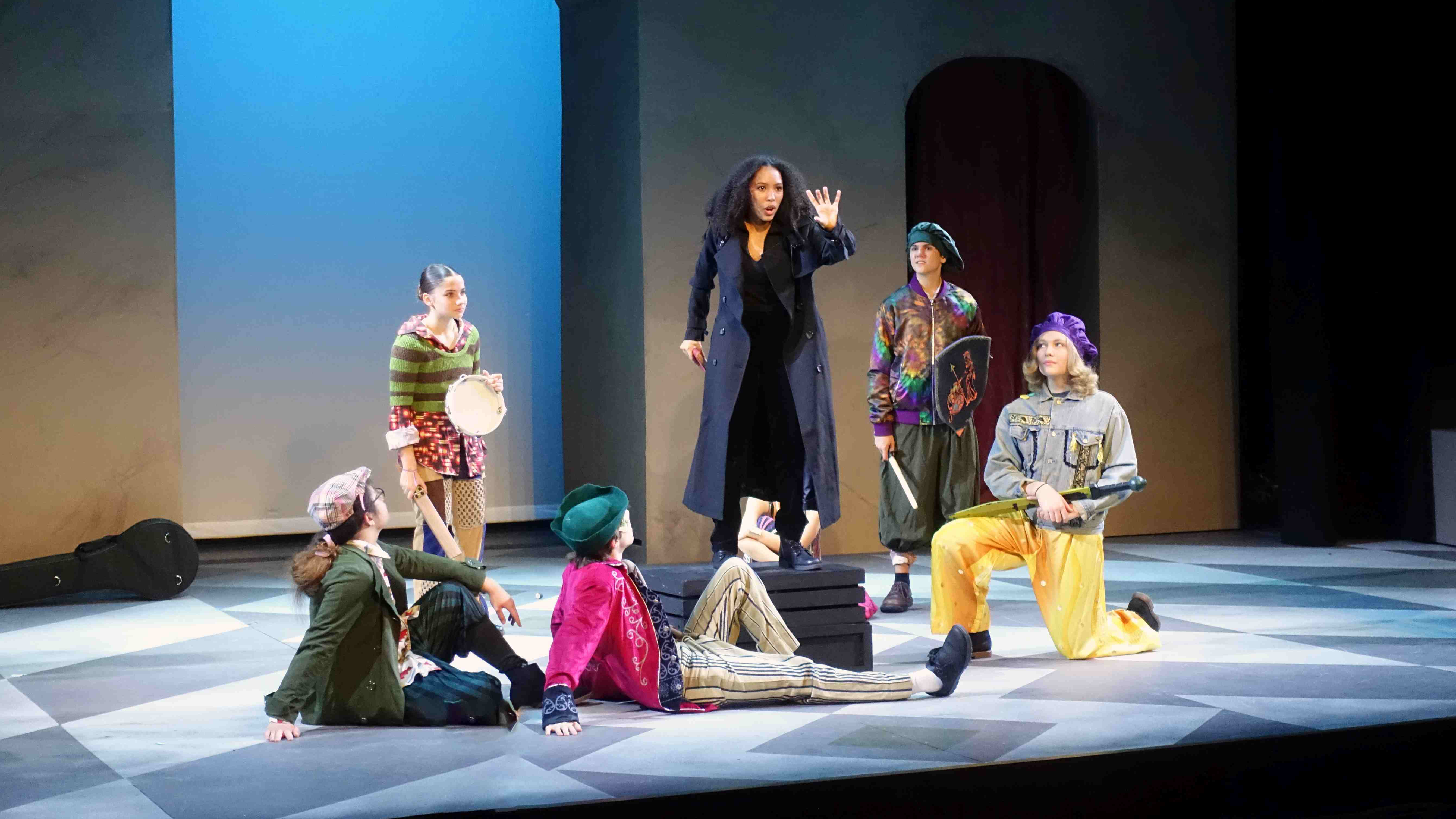 A group of actors perform on stage in colorful costumers.