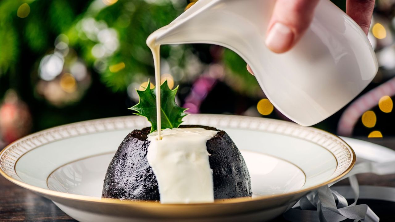 a jug pouring brandy sauce over a plate of Christmas pudding