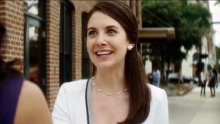 Alison Brie, wearing white and smiling big as Sydney Prescott's publicist Rebecca Walters in Scream 4.