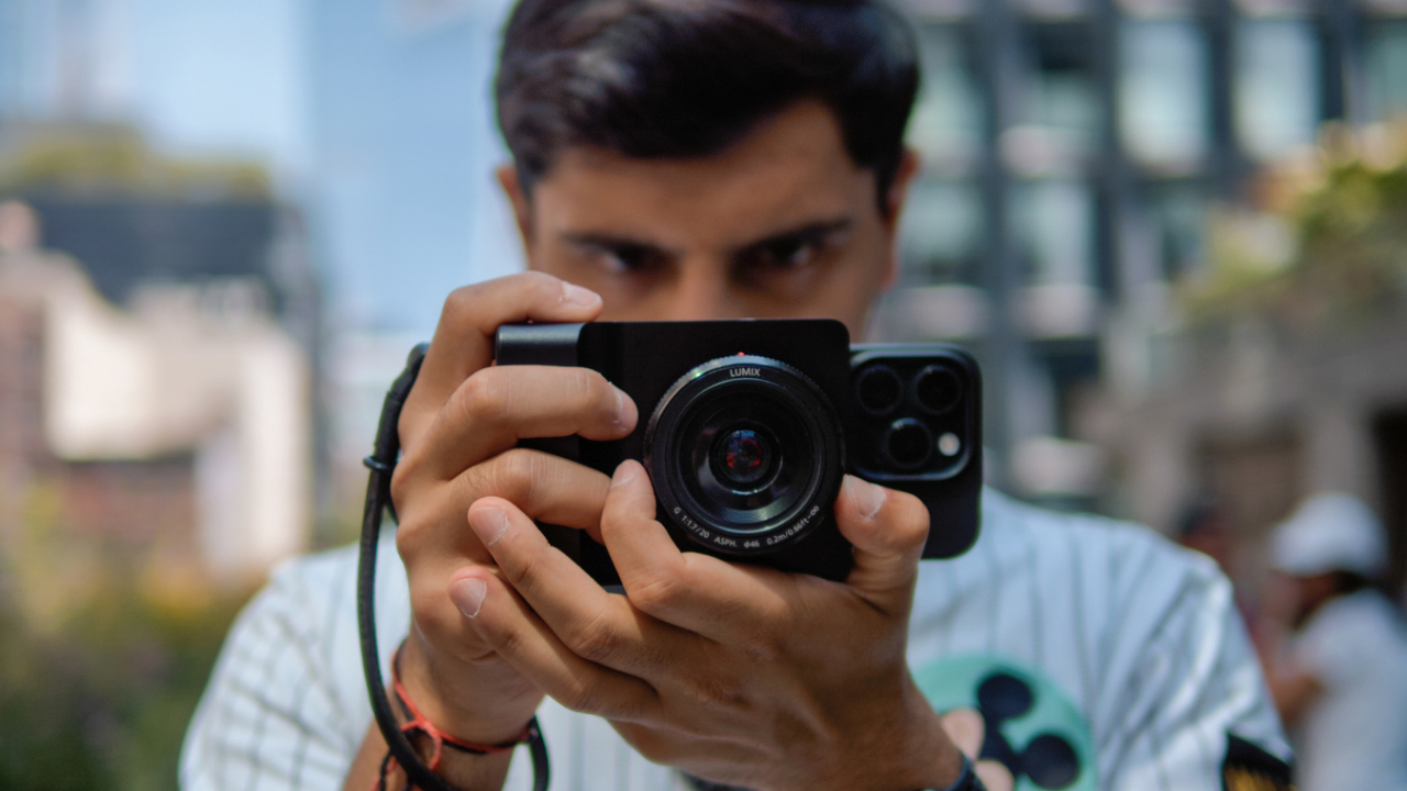 A person holds a mirrorless camera with a smartphone on the back