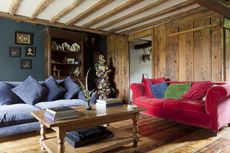 wooden walled living room with beams and red and blue velvet sofas and wooden floors