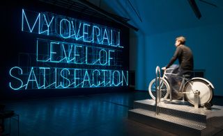 Pic 3 of 3 - man on a bicycle in front of a neon sign reading "MY OVERALL LEVEL OF SATISFACTION"