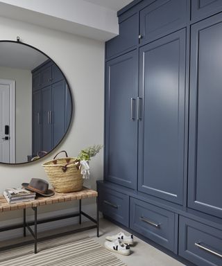 A mudroom with a wall of navy blue cabinets, bench and large wall mirror