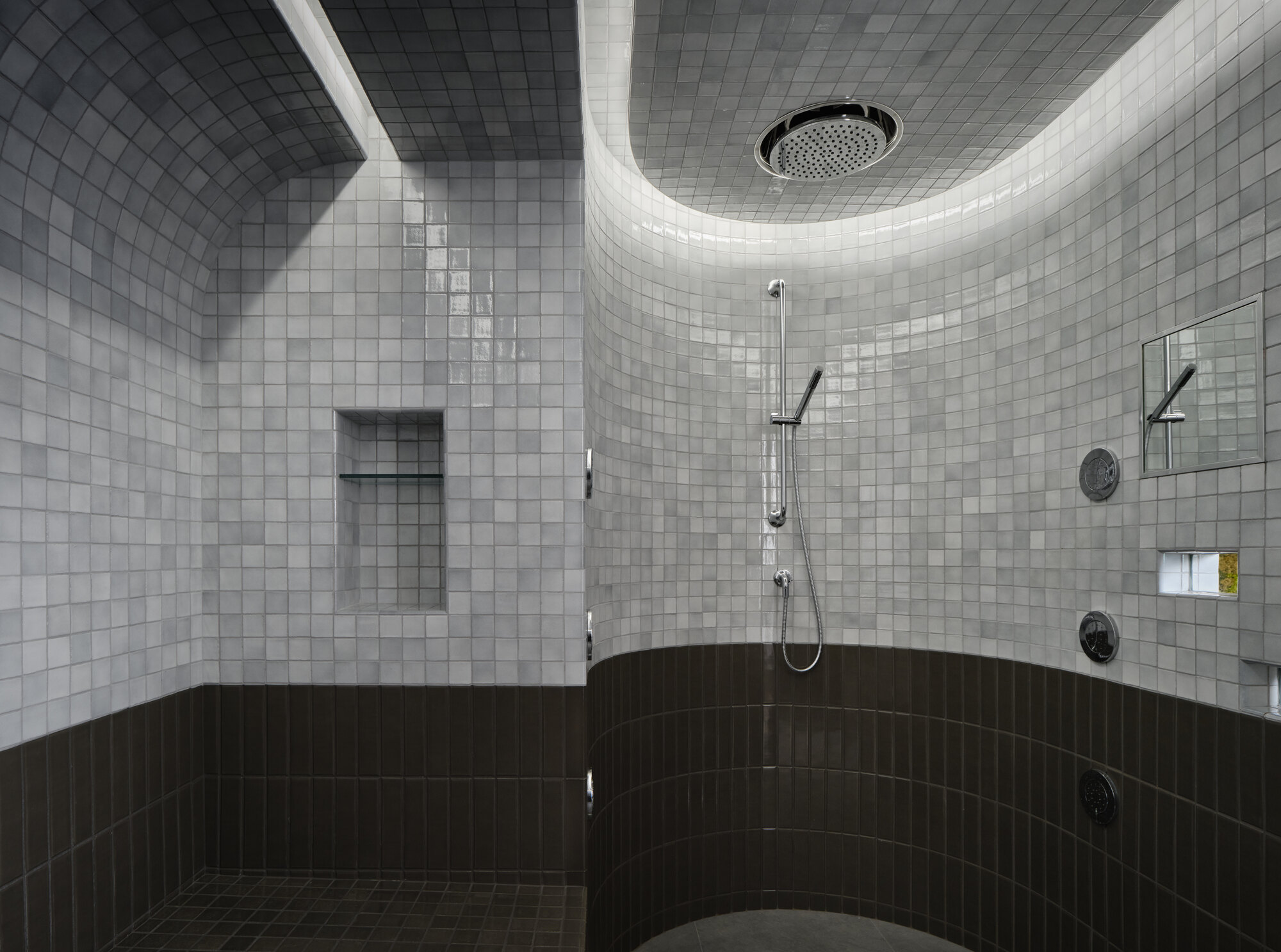 large tiled steam shower with gray and black tiles, curved walls and LED lighting around the ceiling with silver tapware and shower niche