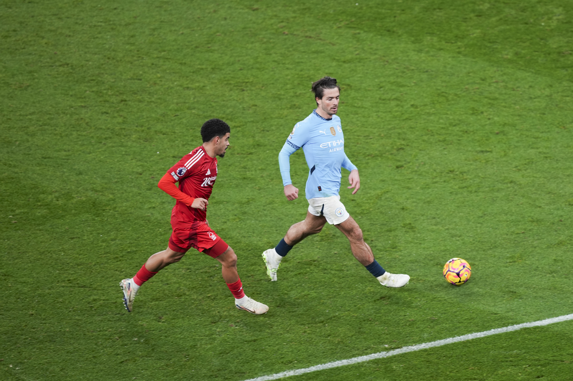 Manchester City player Jack Grealish kicking ball during Premier League match, tracked by Morgan Gibbs-White