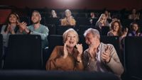 A happy elderly couple applauding in a movie theater. 