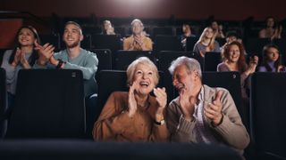 A happy elderly couple applauding in a movie theater.