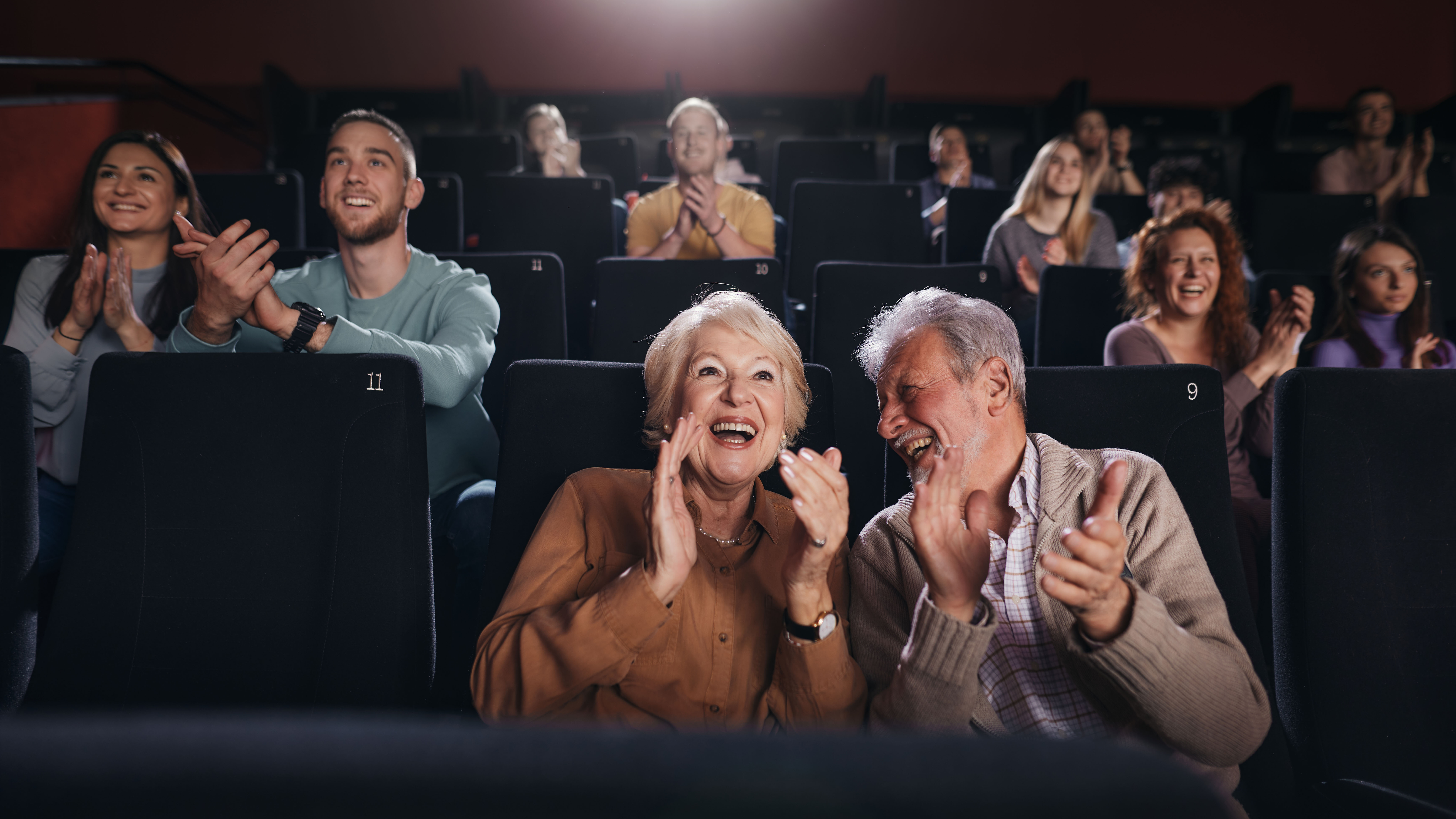 A happy elderly couple applauding in a movie theater.