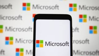 Image of Microsoft logo on a smartphone in front of a white backdrop with many identical Microsoft logos sprawled across